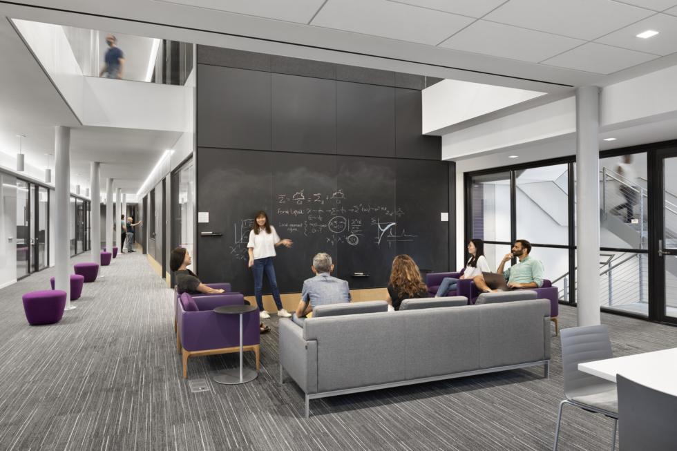 Flatiron Institute New York: The common area of the two-story quantum physics department, showing the chalkboard core that runs through the building, glass-front perimeter offices, and the main stair.